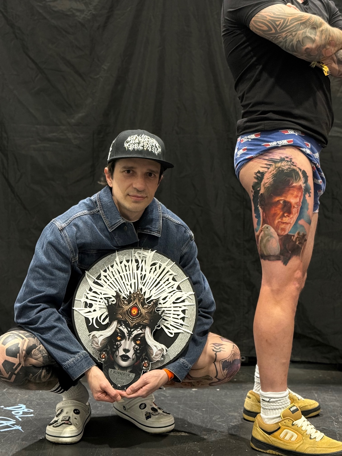 Vladimir Vishar at a tattoo convention next to a client's healed leg tattoo